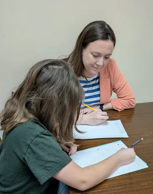 Heather supports a child during a handwriting activity at Together OT